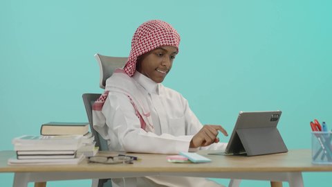 متابعة منصات التعليم الالكتروني المتاحة عبر الانترنت بإستخدام جهاز الحاسوب اللوحي، ادخال التقنية والتكنولوجيا بالتعليم، بورتريه لطالب عربي خليجي سعودي يرتدي الشماغ والثوب التقليدي يقوم باستخدام التابلت, مفهوم الاجتهاد والتفوق, الاستعداد للعام الدراسي الجديد، خلفية زرقاء