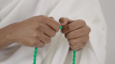 قراءة الأذكار والأدعية، التسبيح والتهليل وذكر الله تعالى، بورتريه مقرب لحاج عربي خليجي سعودي يرتدي لباس الإحرام يمسك بيده سبحة خضراء، التقرب لرب العالمين، التهليل والتسبيح وذكر الله تعالى، طلب المغفرة والدعاء والصفح، الاجتهاد في العبادة, خلفية رمادي