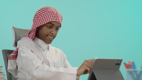 مفهوم التعليم الإلكتروني، مراجعة الدروس اليومية عبر الانترنت، تطور العلم والتعليم في السعودية, بورتريه لشاب عربي خليجي سعودي مبتسم يرتدي الثوب التقليدي و الشماغ يقوم باستخدام الجهاز اللوحي, مفهوم الاجتهاد والتفوق, الاستعداد للعام الدراسي الجديد، خلفية زرقاء