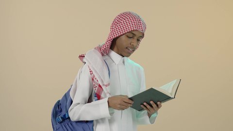 مفهوم الاجتهاد والتفوق, الاستعداد للعام الدراسي الجديد، تحضير الدروس للوصول إلى النجاح, بورتريه لشاب عربي خليجي سعودي يرتدي الثوب التقليدي و شماغ و حقيبة ظهر يقوم بقراءة كتاب, تطوير المناهج التعليمية في السعودية, خلفية بيج