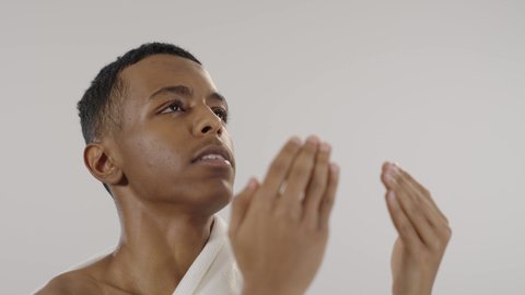 آداء فريضة الحج، موسم العمرة في شهر رمضان المبارك، مفهوم الاجتهاد في العبادة, الدعاء والتقرب الى الله، بورتريه لرجل مسلم عربي سعودي خليجي يرتدي ملابس الاحرام يدعي بتضرع وخشوع ويرفع يديه للأعلى، خلفية رمادية