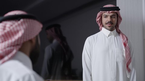 Distribution of work tasks, two Arab Gulf men wearing traditional attire and shemagh are sitting inside the office discussing operational developments, work improvement and problem-solving, unity and teamwork, developing company goals, Saudi work environment.