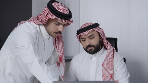 A Saudi Gulf Arab team is in a business meeting at the company's headquarters, discussing the company's goals and policies, explaining the work strategy, discussing a project, training and developing employees, a Saudi work environment, Saudi Gulf Arab companies, managing work using a laptop.