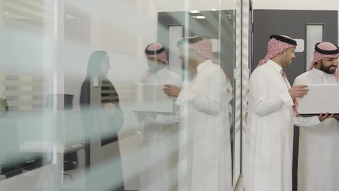 تطوير ودراسة المشاريع الجديدة في المملكة العربية السعودية، اجتماع ومناقشة عمل في مقر الشركة، رجل عربي خليجي سعودي  يرتدي الثوب التقليدي و الشماغ يقوم بالعمل على الحاسب المحمول مع زملاءه داخل الشركة، استخدام جهاز تقني حديث، جمع البيانات وحل المشكلات