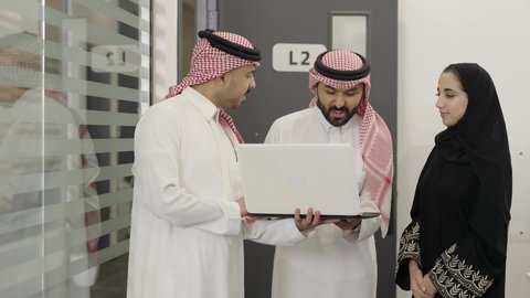 اجتماع ومناقشة عمل في مقر الشركة، رجل عربي خليجي سعودي  يرتدي الثوب التقليدي و الشماغ يقوم بالعمل على الحاسب المحمول مع زملاءه داخل الشركة، تطوير ودراسة المشاريع الجديدة في المملكة العربية السعودية، استخدام جهاز تقني حديث، جمع البيانات وحل المشكلات