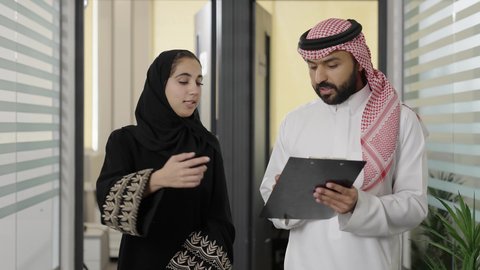 التفاهم والتعاون بين الزملاء لتحقيق الاهداف، إنجاز الأعمال المكتبية، كتابة وتسجيل البيانات والملاحظات، تطوير خطة وآلية العمل، التحقق والتدقيق في العروض المالية، رجل عربي خليجي سعودي يرتدي الزي التقليدي و الشماغ يقوم بشرح المهام لزميلته داخل الشركة