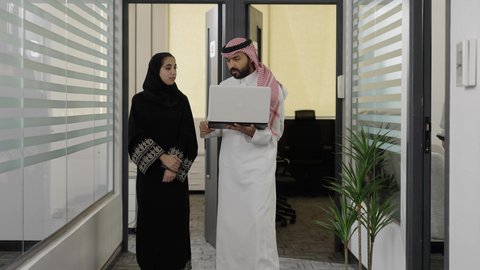 تبادل الأفكار والخبرات لتطوير استراتيجيات العمل، زميلين عربيين خليجيين سعوديين  يسيريان داخل الشركة يقومان بإنجاز المهام عبر الحاسوب المحمول، التعاون وتوحيد الجهود لتحقيق أهداف الشركة، دمج التقنية و التكنولوجيا في العمل