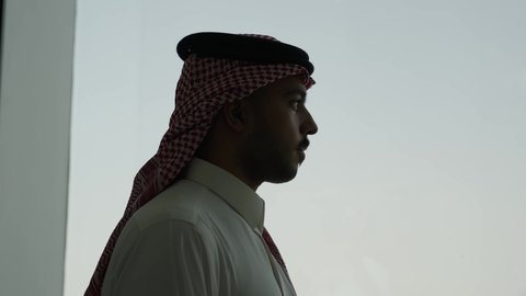 Tourist landmarks in Riyadh, architectural engineering arts of skyscrapers in the Kingdom of Saudi Arabia, famous commercial buildings and towers, urban growth and development, a side shot of a Saudi Arabian Gulf man wearing a shemagh looking out of an office window at the Al-Masmak Tower in the city of Riyadh.