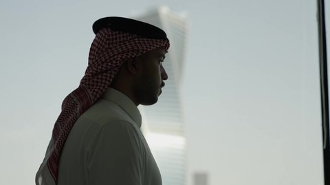 الفنون الهندسية المعمارية لناطحات السحاب في المملكة العربية السعودية، المباني والأبراج التجارية المشهورة، النمو والتطور العمراني، تصوير ظلى من الجانب لرجل عربي خليجي سعودي يرتدي الشماغ ينظر من نافذة المكتب على برج المجدول في مدينة الرياض ، معالم الرياض السياحية