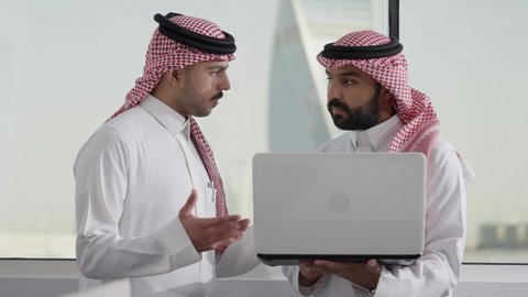 تدريب الموظفين الأساليب الجديدة في العمل لتحقيق أهداف الشركة، دمج العمل مع التقنية والتكنولوجيا، زميلان عربيان خليجيان سعوديان يرتديان الزي التقليدي و الشماغ يقومان بإنجاز المهام عبر الحاسوب المحمول، الاشارة الى اللابتوب، العمل الجماعي وروح الفريق الواحد، بيئة العمل المريحة في السعودية