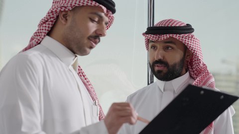 العمل الجماعي وروح الفريق الواحد، التفاهم والتعاون بين الزملاء ووضع الخطط الاستراتيجية لتحقيق الأهداف، ضمان فهم واضح وشامل للاعمال،  تصوير مقرب لموظفان عربيان خليجيان سعوديان يرتديان الثوب التقليدي و الغتره يعقدون اجتماع داخل مقر الشركة، تعلم اساليب العمل والتطوير المهن، تدووين الملاحظات و تسجيلها