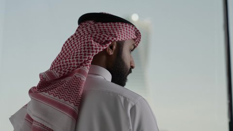 الفنون الهندسية المعمارية لناطحات السحاب في المملكة العربية السعودية، النمو والتطور العمراني،  تصوير مقرب من الخلف لرجل عربيى خليجي سعودي يرتدي الشماغ ينظر من نافذة المكتب على برج المجدول في مدينة الرياض ، معالم الرياض السياحية، المباني والأبراج التجارية المشهورة
