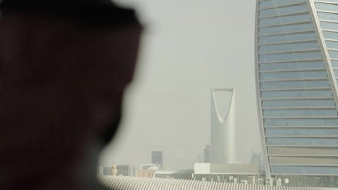 Urban growth and development, a close-up shot from behind of a Saudi Arabian Gulf man wearing a ghutrah looking out of an office window at the Al-Majdoul Tower in Riyadh, the architectural engineering arts of skyscrapers in the Kingdom of Saudi Arabia, the tourist landmarks of Riyadh, famous commercial buildings and towers.