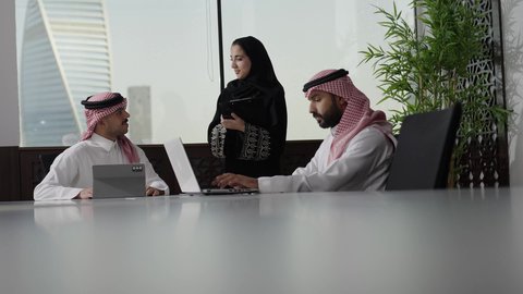 تطوير ودراسة المشاريع الجديدة في المملكة العربية السعودية، استخدام جهاز تقني حديث، جمع البيانات وحل المشكلات، اجتماع ومناقشة عمل في مقر الشركة، رجل أعمال عربي خليجي سعودي يرتدي الثوب الابيض و الشماغ يقوم بالعمل على الحاسب المحمول مع زملاءه داخل المكتب