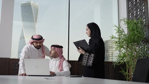 تطوير ودراسة المشاريع الجديدة في المملكة العربية السعودية، استخدام جهاز تقني حديث، جمع البيانات وحل المشكلات، اجتماع ومناقشة عمل في مقر الشركة، رجل أعمال عربي خليجي سعودي يرتدي الثوب الابيض و الشماغ يقوم بالعمل على الحاسب المحمول مع زملاءه داخل المكتب