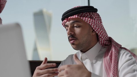 Use modern technologies in administrative work, a close-up shot of a Saudi Gulf Arab man wearing a ghutrah working on a laptop, making video calls, integrating advanced technology into daily life.