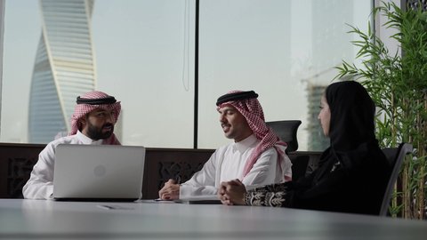 Monitoring and discussing the company's strategies and goals, dialogues and discussions in the work environment, Arab Saudi Gulf employees wearing traditional attire and the ghutrah sitting in the meeting room inside the company's headquarters, Saudi professions and jobs, a Saudi work team, completing required tasks via laptop, integrating technology into work.
