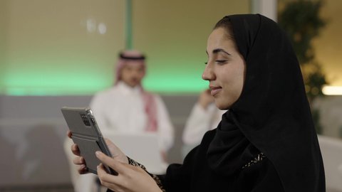 اجراء مكالمة فيديو عبر التابلت، استخدام الأجهزة التقنية الحديثة،عقد إجتماع عمل عبر الإنترنت، تصفح مواقع التواصل الاجتماعي، التواصل مع الأهل والأصدقاء عبر الايباد، تصوير مقرب من الجانب لإمرأة عربية خليجية سعودية محجبة ترتدي العباءة السوداء تقوم باستخدام الجهاز اللوحي