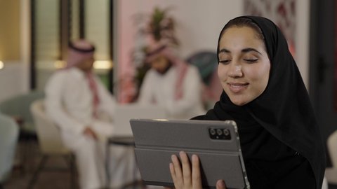 Communicating with family and friends via the iPad, browsing social media sites, using modern technological devices, the concept of completing projects and tasks while working remotely, a close-up shot of a Saudi Arabian Gulf woman wearing a black abaya and using a tablet.