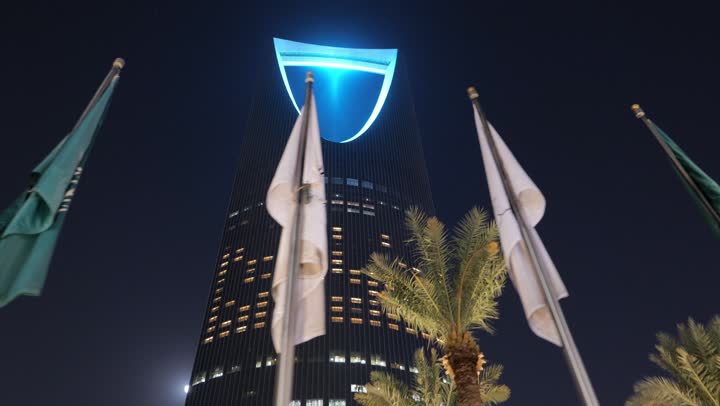 Famous tourist attractions and places that attract visitors from all over the world, the advanced architectural art of the illuminated Kingdom Tower building in the Saudi capital, the development of modern engineering facilities in the Kingdom, skyscrapers at night in the city of Riyadh, green palm trees