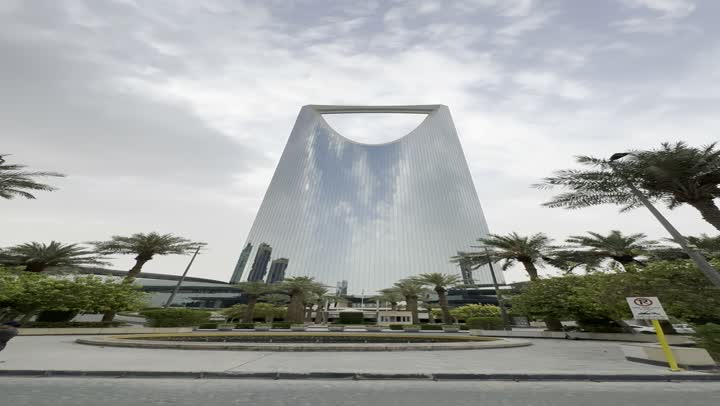 Green palm trees in the area of the famous Kingdom Tower in Riyadh, popular tourist spots and landmarks that attract visitors from all over the world, the evolution of architectural engineering in a modern style, towers and skyscrapers, daytime photography of a famous landmark in the capital.