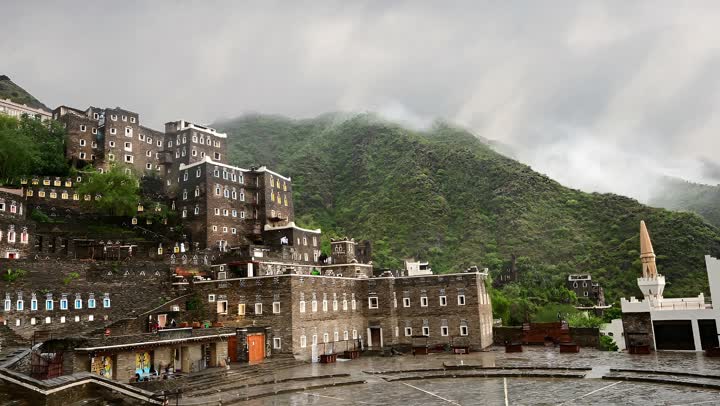 Stone buildings with wooden windows, the architectural engineering art of old-style buildings in the city of Abha, famous landmarks and tourist attractions in the Kingdom of Saudi Arabia, the archaeological village of Rijal Almaa in the Asir region, attracting and drawing tourists from around the world, the foggy atmosphere over the mountains.
