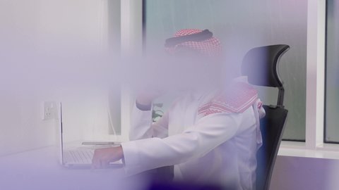 ايماءات الغضب خلال اتصال هاتفي باستدام الجهاز المحمول، متابعة الأعمال عبر الاونلاين, انهاء المهام المكتبية عبر التقنيات الالكترونية الحديثة والمتطورة,  رجل عربي خليجي سعودي يرتدي الثوب التقليدي والشماغ بجانبه حاسب محمول على المكتب، وظائف ومهن مكتبية سعودية