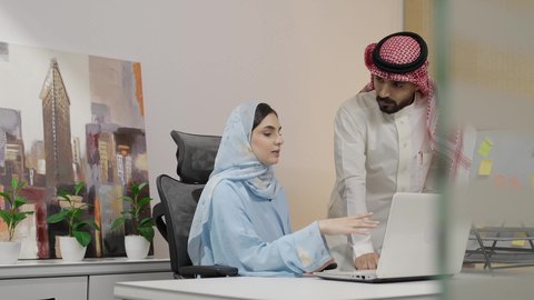 إدارة شؤون الأعمال وتنظيمها عبر الاجهزة الحديثة ، دمج التقنيات المتطوره فى الحياه اليوميه ،إمرأة عربية خليجية سعودية ترتدي العباءة والحجاب تقوم بشرح معلومات العمل ، المشاركة والتعاون وتبادل الآراء بين زملاء العمل، رجل سعودي يقوم  بالاستماع والتركيز