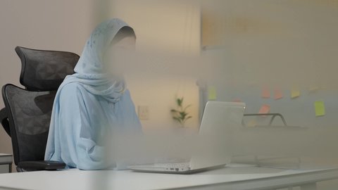 مفهوم الاناقة والاهتمام بالمظهر الخارجي، سيدة سعودية تدون الملاحظات على الحاسب المحمول، وظيفة مكتبية في شركات الخليج العربي، تحليل نتائج البيانات الاحصائية، امراة عربية خليجية سعودية محجبة ترتدي العباءة تجلس خلف الطاولة تعمل لانجاز المهام في المكتب