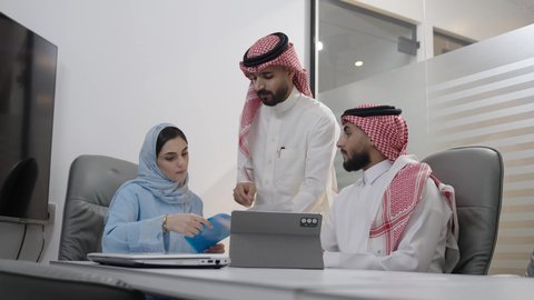 Discussions and dialogues to achieve strategies and goals, a work meeting among Saudi Gulf Arab employees in the meeting room, understanding and cooperation among colleagues to achieve the company's objectives, a comfortable work environment in Saudi companies, the use of modern technological devices in offices.