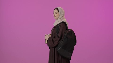 Education in the Kingdom of Saudi Arabia, gestures of self-confidence, a portrait of a Saudi Arabian Gulf student wearing an abaya and a backpack, holding a collection of books in her hands, looking at the camera with gestures of happiness and joy, colorful background.