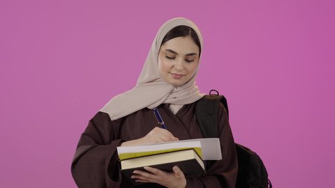 مذاكرة المحاضرات الجامعيه, قراءة الدروس اليوميه, التعليم في المملكه العربيه السعوديه، بورترية لطالبة عربيه خليجيه سعودية ترتدي العباءة و تحمل حقيبه الظهر تقوم بكتابة شيء ما ، ايماءات التذكر و التفكير ، خلفية ملونه