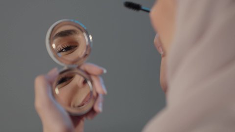 Makeup tutorial training courses, using mascara to enhance the beauty of the eyes, caring about beauty and appearance, women's cosmetics, a close-up portrait from the back of a Saudi Gulf Arab woman applying makeup, gray background.
