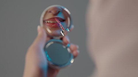 العناية بالإطلالة والجمال الشخصي، الترويج لمنتجات و مساحيق التجميل، استعمال المستحضرات التجميلية، مفهوم التزين والتجمل, بورتريه مقرب ليد امراةعربية خليجية سعودية تضع أحمر شفاه, خلفية رمادية