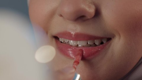 استعمال المستحضرات التجميلية، مفهوم التزين والتجمل, الترويج لمنتجات و مساحيق التجميل, العناية بالجمال والمظهر الخارجي, بورتريه مقرب لامرأة عربية خليجية سعودية محجبة  تضع أحمر شفاه, خلفية رمادية