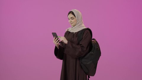 Using a modern advanced technical device, displaying a mobile phone with a green screen, the importance of university education, a portrait of a Saudi Arabian Gulf university student wearing a hijab, dressed in an abaya and carrying a school bag, holding a mobile phone in her hand, with a colorful background.