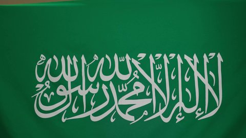 الاحتفال بالعيد الوطني لتوحيد السعودية على يد الملك عبد العزيز في 8 ربيع الأول، يوم العلم السعودي 11 مارس، اليوم الوطني السعودي،سيدة عربية خليجية سعودية مبتسمة محجبة ترتدي العباءة السوداء ترتدي علم المملكة بتعابير الفخرو السرور، خلفية بني