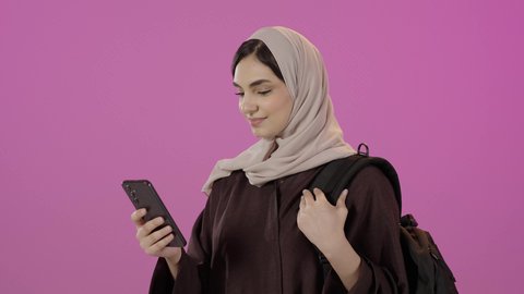 A mobile phone display with a green screen, the importance of university education, using a modern advanced technical device, a close-up portrait of a Saudi Arabian Gulf university student wearing a hijab, dressed in an abaya and carrying a school bag, holding a mobile phone in her hand, colorful background.