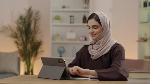 حل الواجبات الالكترونية، متابعة المحاضرات الجامعية الالكترونية عبر الجهاز اللوحي، طالبة عربية خليجية سعودية محجبة ترتدي العباءة تستخدم جهاز التابلت، كتابة وتدوين الملاحظات، التعليم في المملكة العربية السعودية، ايماءات السعادة و السرور