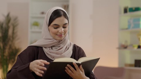 مراجعة الدروس اليومية، مفهوم الاجتهاد والتفوق والنجاح, تصوير مقرب لطالبة جامعية عربية خليجية سعودية محجبة ترتدي العباءة تقوم بمذاكرة الكتاب الجامعي، ايماءات التركيز و الاندماج