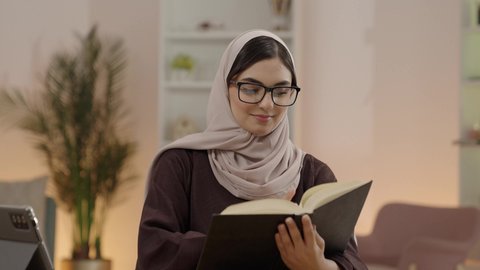 مفهوم الاجتهاد والتفوق والنجاح, مراجعة الدروس اليومية, طالبة جامعية عربية خليجية سعودية محجبة ترتدي العباءة و نظارة قراءة تقوم بمذاكرة الكتاب الجامعي، ايماءات التركيز و الاندماج