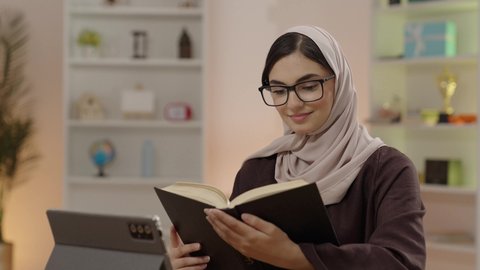 التعليم والتعلم في الكليات السعودية, طالبة جامعية عربية خليجية سعودية محجبة ترتدي نظارة قراءة تقوم بمذاكرة الكتاب الجامعي, الأكاديميات التعليمية في دول الخليج، ايماءات التركيز و الاندماج