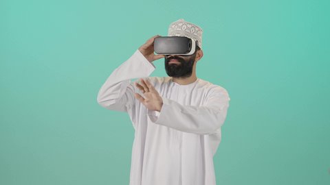 التطور التقني والتكنولوجي, المتعة و التسلية بالمشاهدة عبر نظارة الواقع الافتراضي، بورتريه مقرب لشاب عربي خليجي عماني يرتدي الدشداشه والكمه ينظر من خلال نظارات ثلاثية الأبعاد (الفي ار), الاندماج ومحاكاة العالم الخيالي والنظر الى الافلام الواقعيه، خلفيه زرقاء