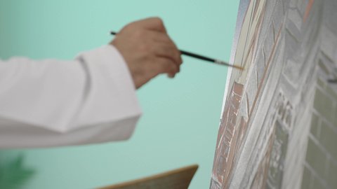 Fun recreational activities, spending enjoyable times, developing and enhancing artistic skills, strengthening abilities and talents, spending free time practicing a favorite hobby, a close-up portrait of the hand of an Arab Gulf Omani man wearing a dishdasha holding a paintbrush using oil colors, blue background.