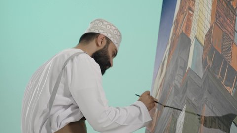 قضاء اوقات ممتعه، تنمية وتطويرالمهارات الفنية التشكيلية، تعزيز القدرات والمواهب، أنشطة ترفيهية مسلية، قضاء اوقات الفراغ بممارسة الهواية المفضلة، بورتريه مقرب لرجل عربي خليجي عماني يرتدي الدشداشة و الكمة يحمل ريشة الرسم باستخدام الألوان الزيتية،  خلفية زرقاء