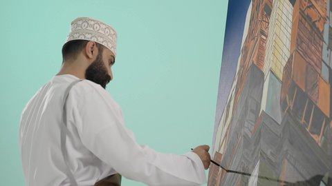 تنمية وتطويرالمهارات الفنية التشكيلية، تعزيز القدرات والمواهب، أنشطة ترفيهية مسلية، قضاء اوقات ممتعه، قضاء اوقات الفراغ بممارسة الهواية المفضلة، بورتريه مقرب لرجل عربي خليجي عماني يرتدي الدشداشة و الكمة يحمل ريشة الرسم باستخدام الألوان الزيتية،  خلفية زرقاء