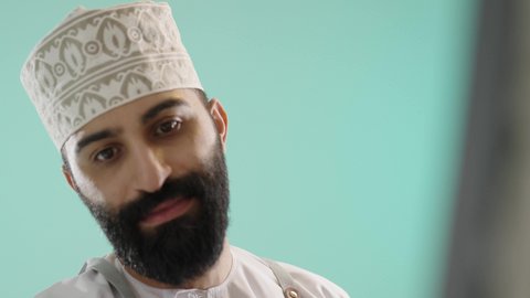 تعزيز القدرات والمواهب،  تنمية وتطويرالمهارات الفنية التشكيلية، أنشطة ترفيهية مسلية، قضاء اوقات ممتعه، قضاء اوقات الفراغ بممارسة الهواية المفضلة، بورتريه مقرب لرجل عربي خليجي عماني يرتدي الدشداشة و الكمة يحملريشة الرسم باستخدام الألوان الزيتية،  خلفية زرقاء