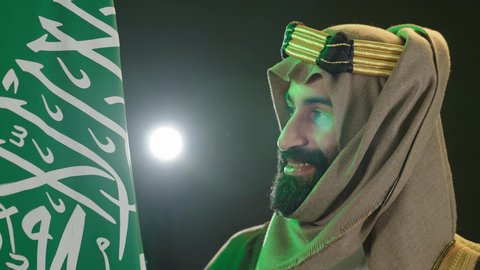 بورتريه  لرجل عربي سعودي خليجي يرتدي البشت والغتره وعقال يوم التأسيس يرفع علم السعوديه، يوم بدينا 1727م ،تذكار اليوم الوطني السعودي 23 سبتمبر، ذكرى تأسيس الدولة السعودية الأولى في 22 فبراير،  يوم العلم ١١ مارس