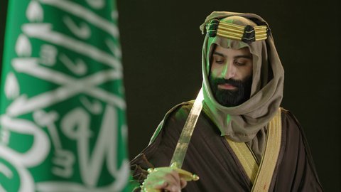 ذكرى تأسيس الدولة السعودية الأولى في 22 فبراير، يوم العلم ١١ مارس ، تذكار اليوم الوطني السعودي 23 سبتمبر، بورتريه  لرجل عربي سعودي خليجي يرتدي البشت والغتره وعقال يوم التأسيس يحمل بيده سيف ويقف بجانب علم السعوديه ، يوم بدينا 1727م
