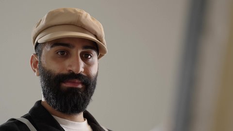 Using drawing and painting tools and equipment, mastering the hobby of handicrafts, art workshop, close-up portrait of a Saudi Arabian Gulf artist wearing traditional clothing and a painting apron sitting on a chair in front of the painting, gestures of joy and happiness